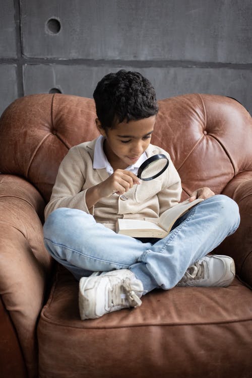 A boy reading book with magnifying glass